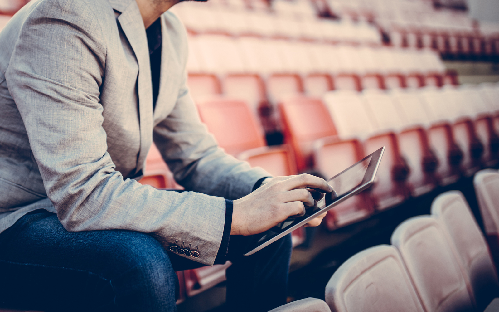 Young and successful football manager working on a tablet, and sitting on the stands alone. Cropped photo.