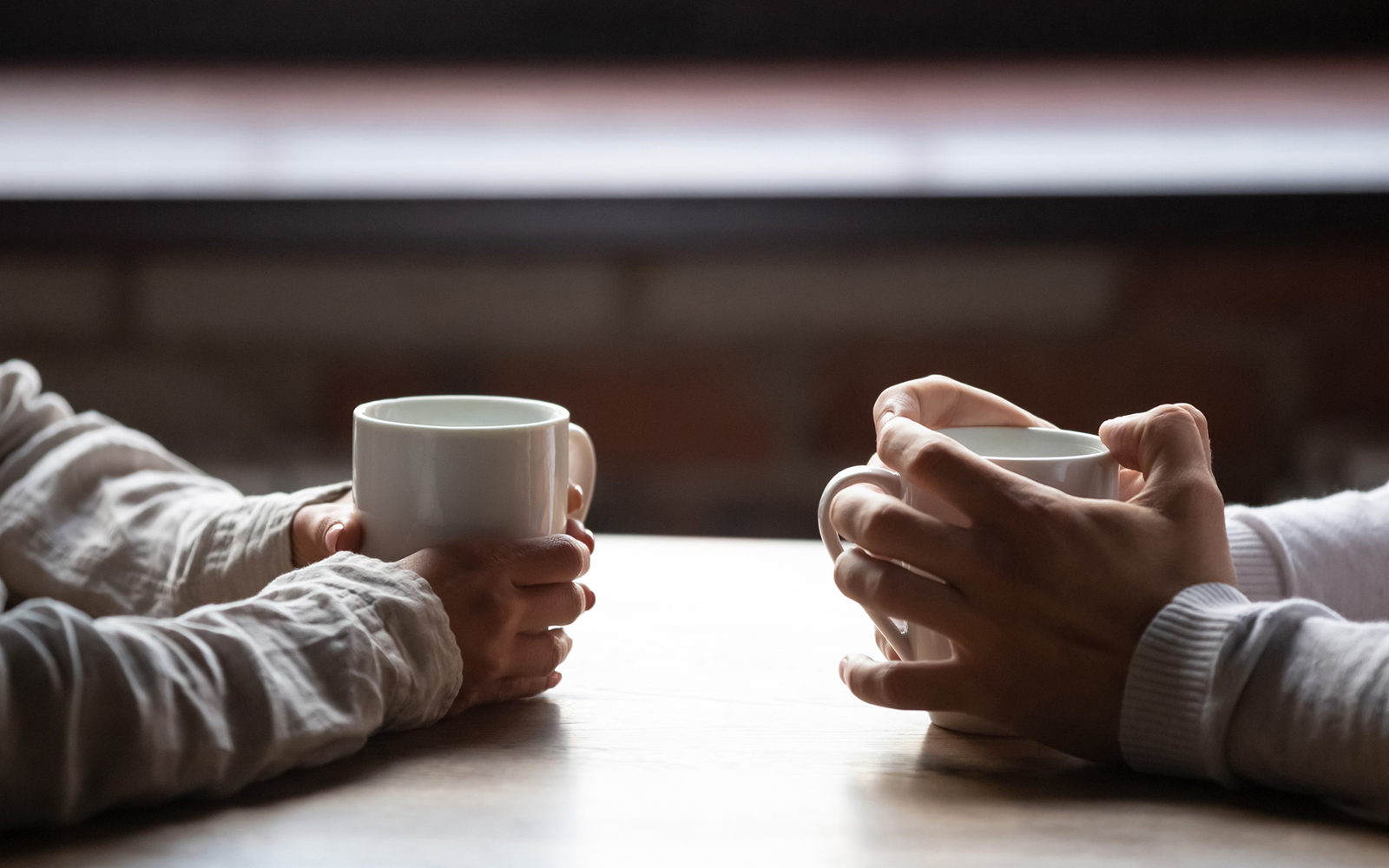 Close up woman and man sitting in cafe, holding warm cups of coffee on table,
