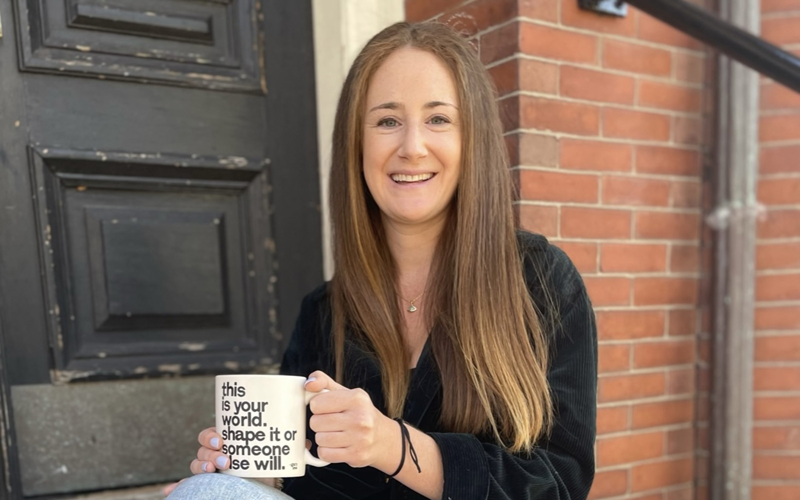 UConn School of Business alumna and entrepreneur Michelle Wax '14 poses on a stoop with a coffee mug