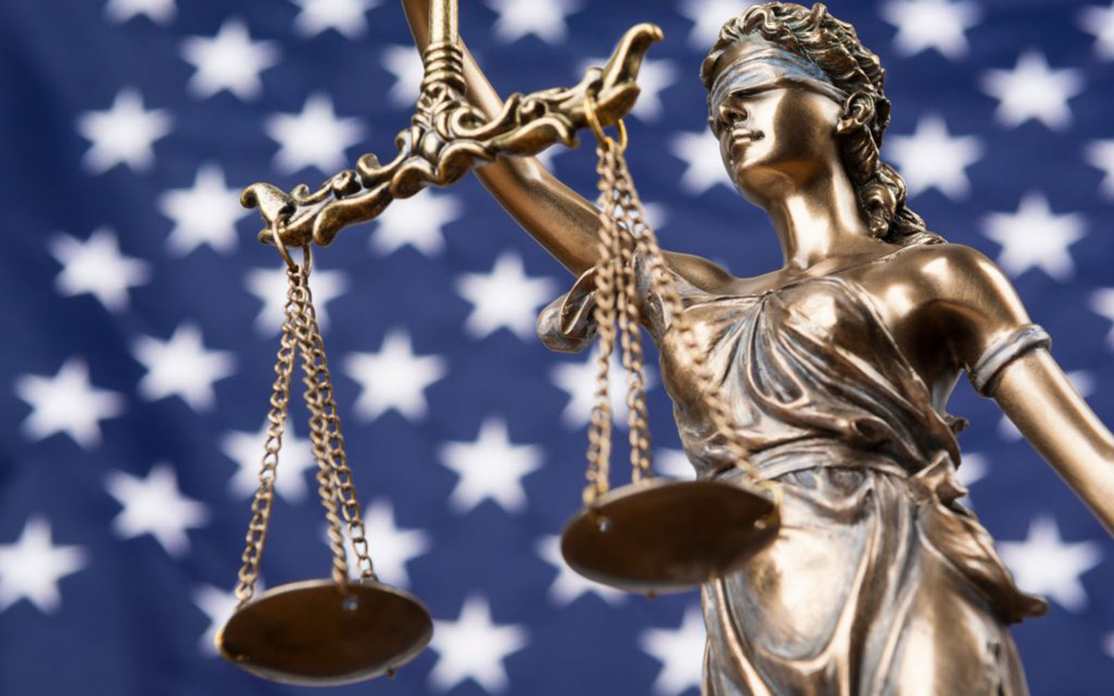 The statue of justice Themis or Justitia, the blindfolded goddess of justice against a flag of the United States of America.