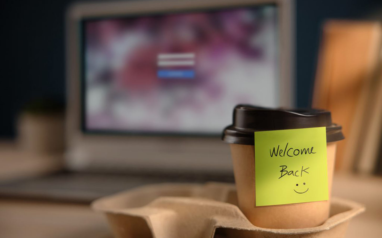 A takeout coffee cup on a desk with a post-it note that says "Welcome Back."