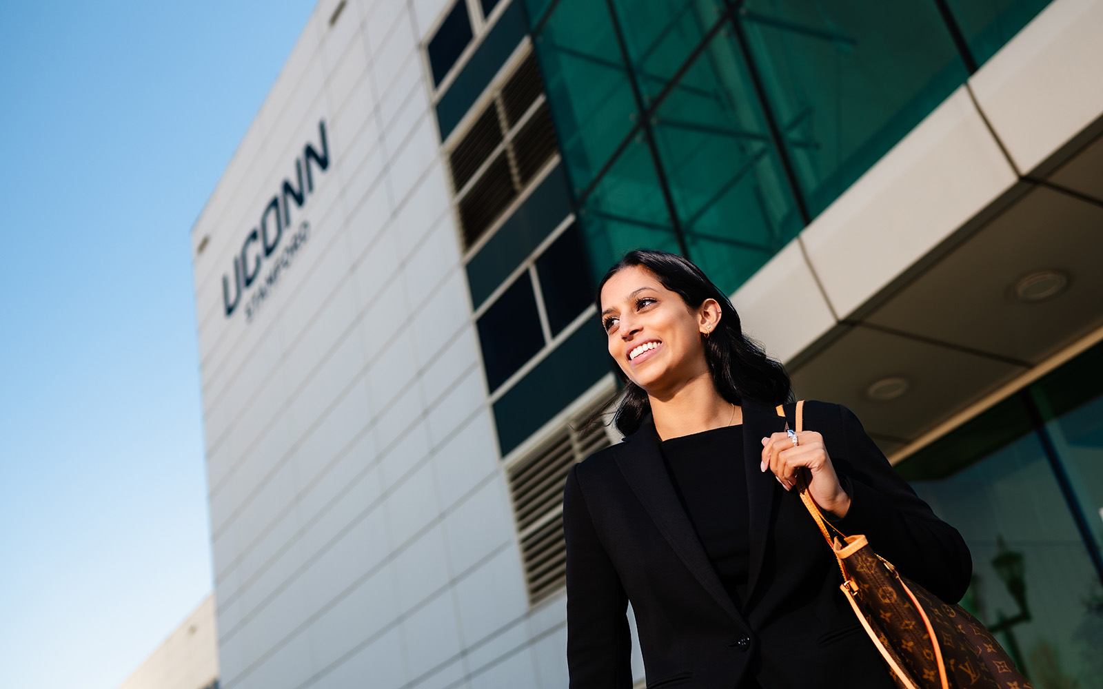 A woman stands in front of the UConn Stamford building.