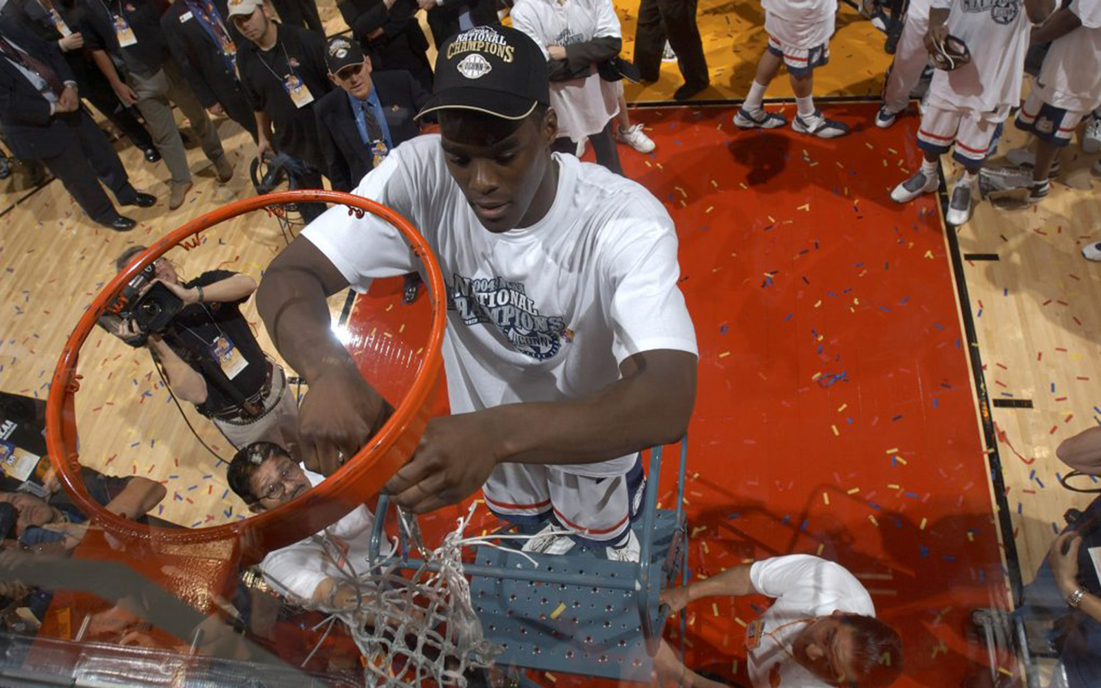 Emeka Okafor stands on a ladder and cuts down a basketball net.