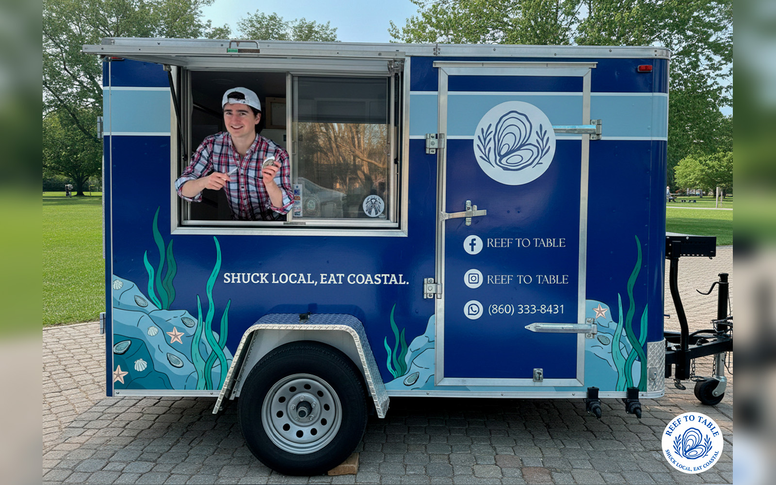 A man points to an oyster in his left hand while he stands at the counter of a food truck.