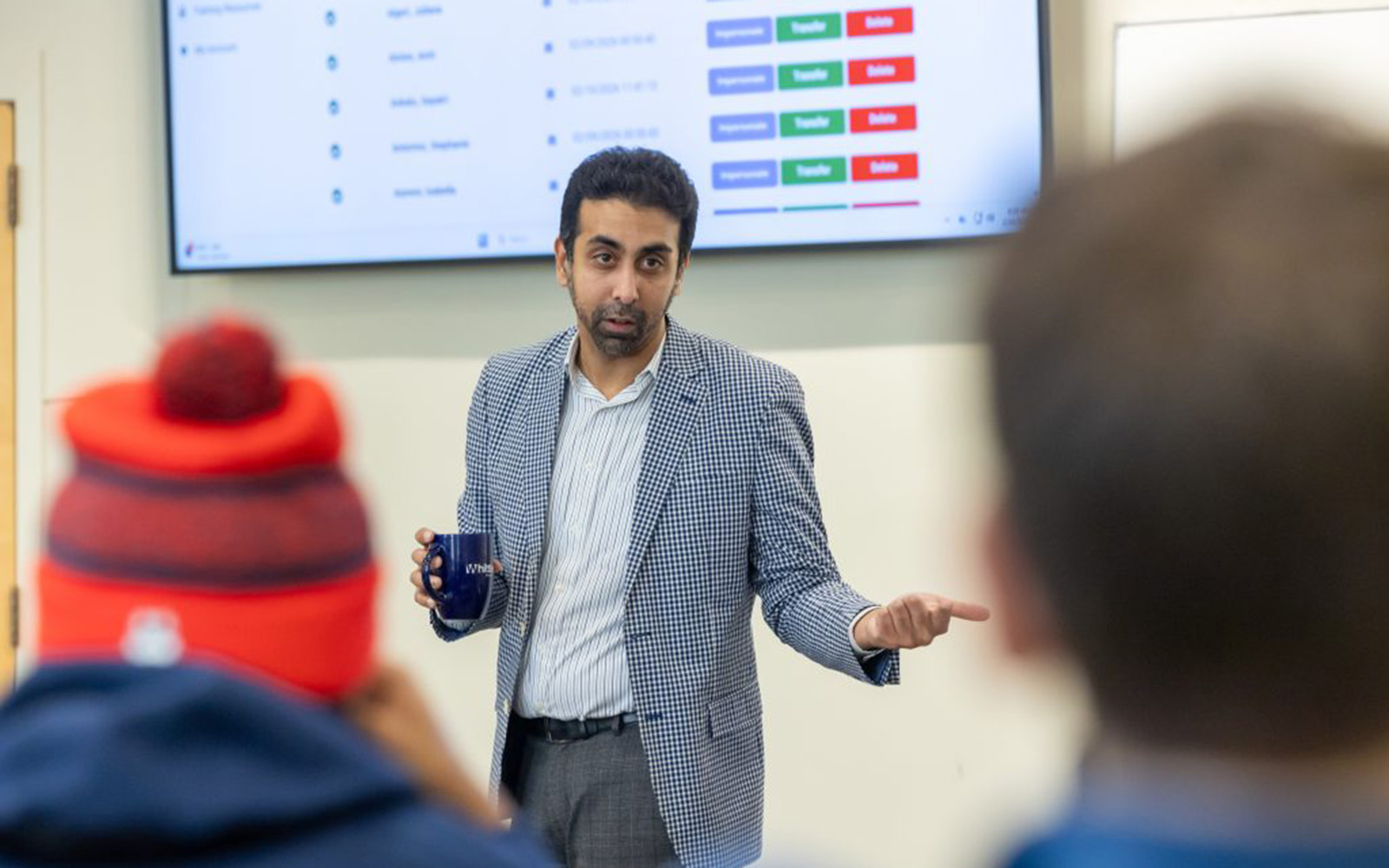 A university professor holding a coffee cup speaks to his class.