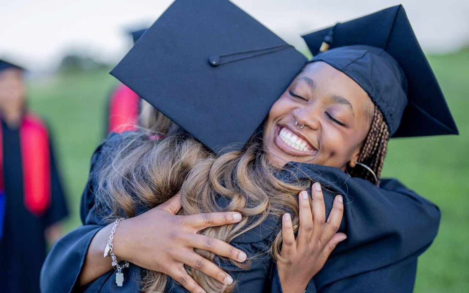 Graduating students dressed in caps and gowns hugging and smiling as they celebrate outdoors