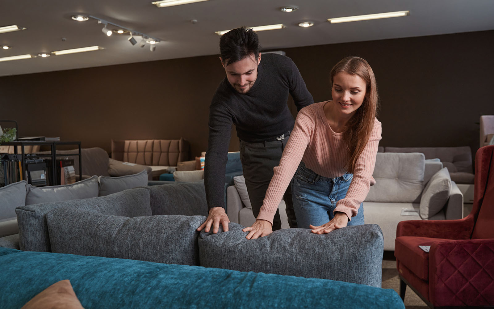 Smiling pleased concentrated young couple assessing upholstery fabric quality by touch