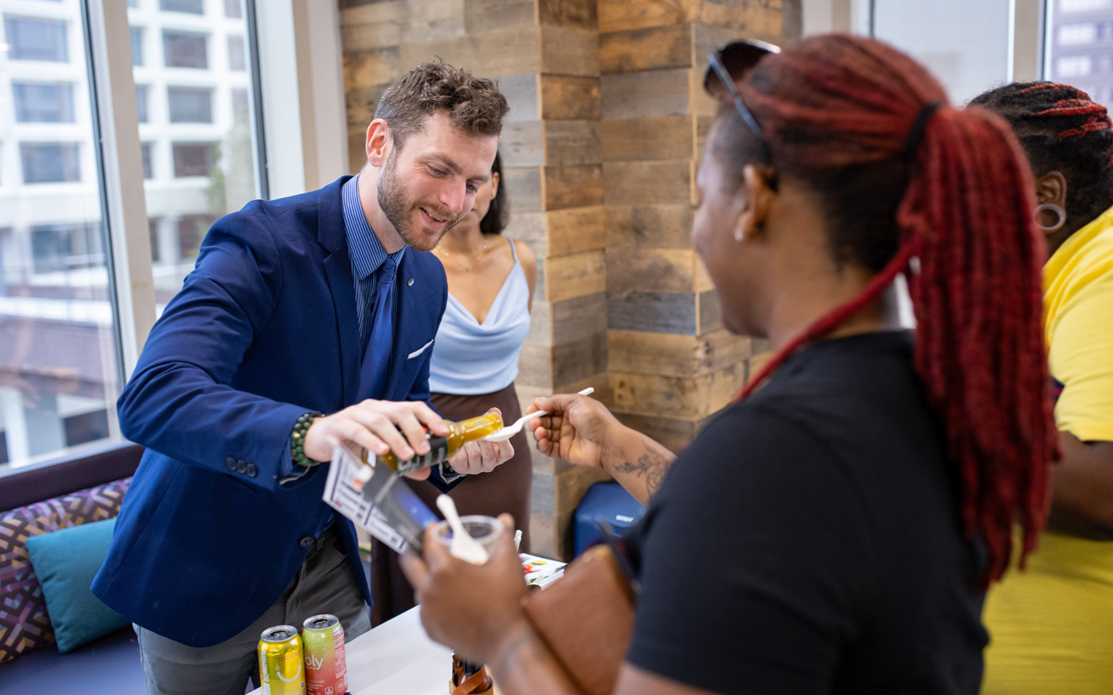 A man puts a sample of hot sauce on a piece of food being held out by a woman.