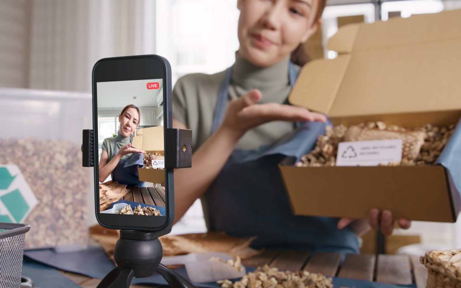 An influencer presents a boxed product to her cell phone camera.
