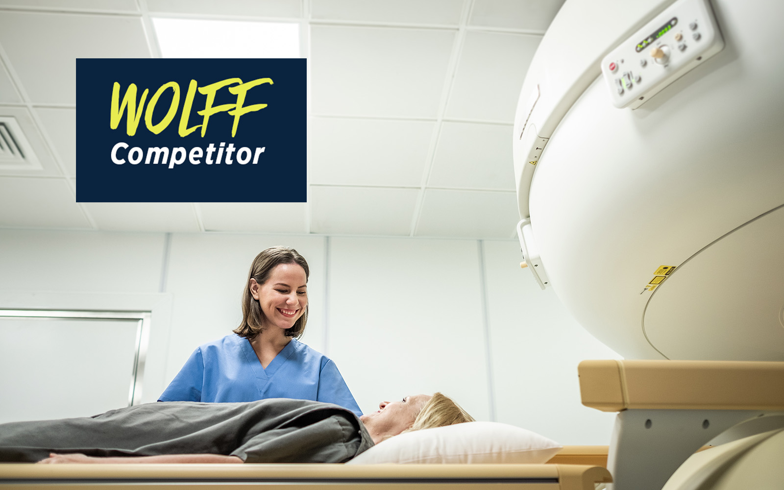 A technician in medical scrubs smiles down at a patient about to be moved into a radiation machine.